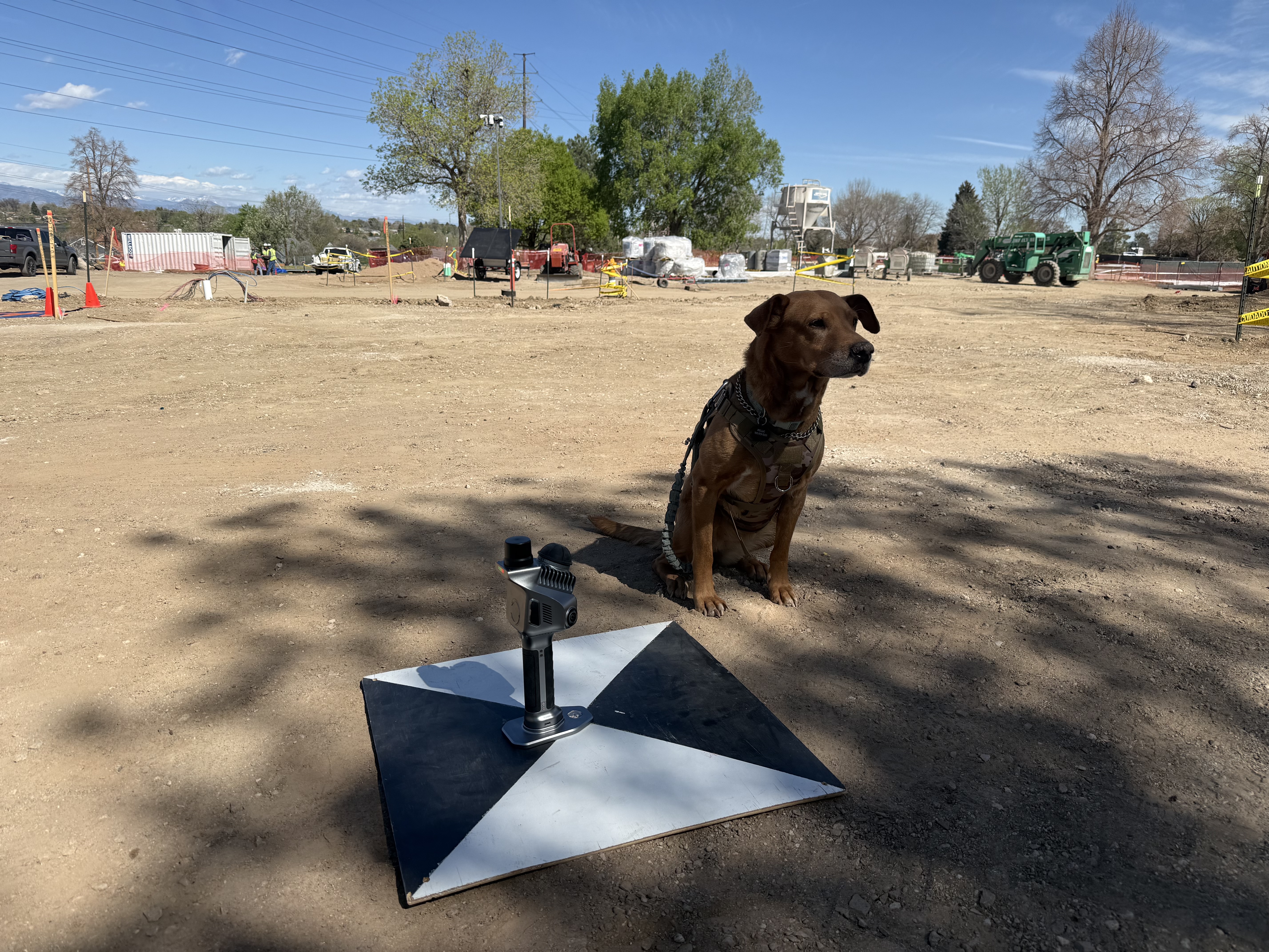 Molle, Michael's service dog, sitting next to his SHARE 20 SLAM scanner and ground control target on a construction site